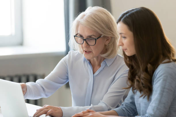 Serious old mentor teaching intern or student pointing at laptop Serious old female mentor teacher coach teaching intern or student computer work pointing at a laptop, mature executive manager explaining online project to young employee learning new skills in office school advisor stock pictures, royalty-free photos & images