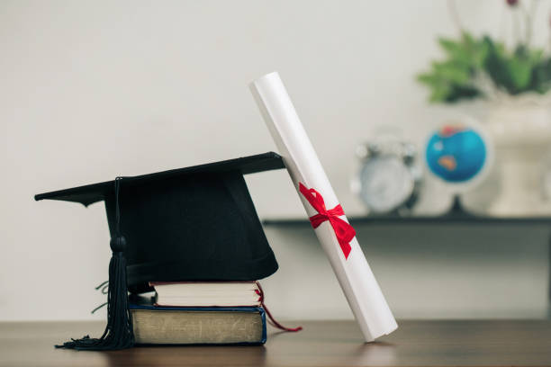 A mortarboard on books and graduation scroll on the desk.education learning concept stock photo