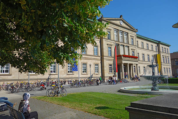 View of the main Tuebingen university building in the Wilhelmstraße Tübingen, Germany - June 17, 2015: View of the main university building in the Wilhelmstraße. The Eberhard Karls University was founded in 1477 and is one of the oldest universities in Europe. On the left side a female muslim student sitting on a bench, many bicycles at the left side of the building and some students at the main entrance.  University of Tübingen stock pictures, royalty-free photos & images