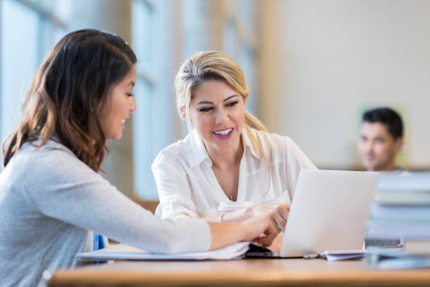 Confident female college students study together for exam Diverse female college students review something on a laptop while studying for an exam. school advisor stock pictures, royalty-free photos & images