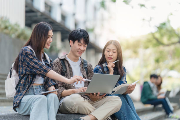 Beautiful young Asian woman college student with friends at outdoors. College student working on the college campus Beautiful young Asian woman college student with friends at outdoors. College student working on the college campus. Reading stock pictures, royalty-free photos & images